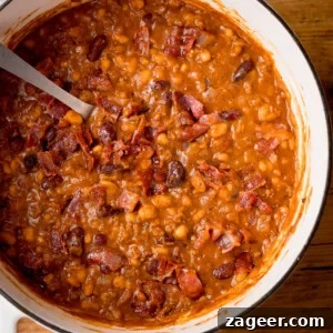 Slow-Cooked Cowboy Beans Recipe with Smoky Bacon and BBQ Flavors 12 Square, close-up, overhead image of cowboy beans in a white casserole dish with a metal spoon sticking out.