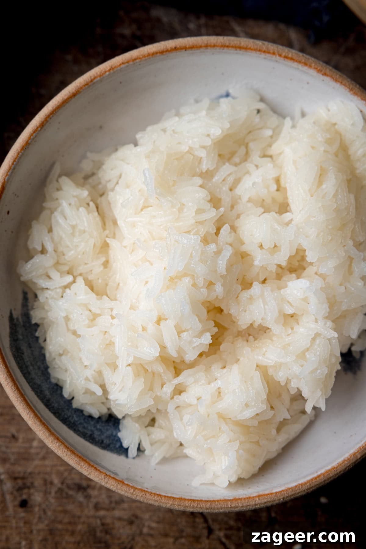 How to Make Perfect Thai Sticky Rice: Rice Cooker & Stovetop Methods 6 A tall, overhead shot of the sticky rice in a large white and blue bowl with a light brown lining. This is set on a dark wooden background.