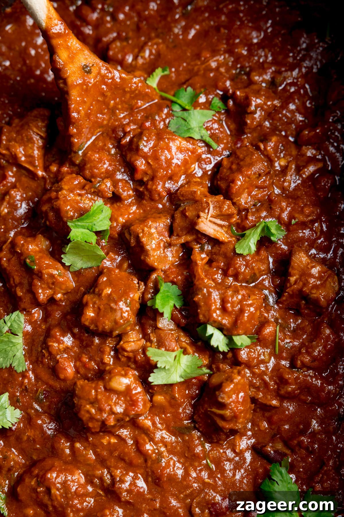 Slow-Cooked Pork and Beef Chili Recipe for Tender, Flavorful Meals 6 Extreme close-up overhead image of slow cooker pork and beef chilli with a wooden spoon sticking out. There is a little sprinkle fresh coriander on top.