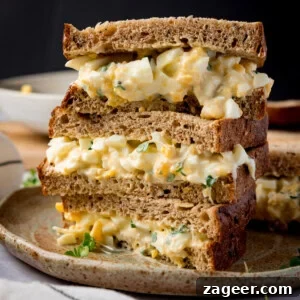 Creamy Egg Mayo Sandwich Recipe for Quick Meals 14 Square side-on image of 3 egg mayonnaise sandwich halves, on brown bread, piled up on a brown plate.
