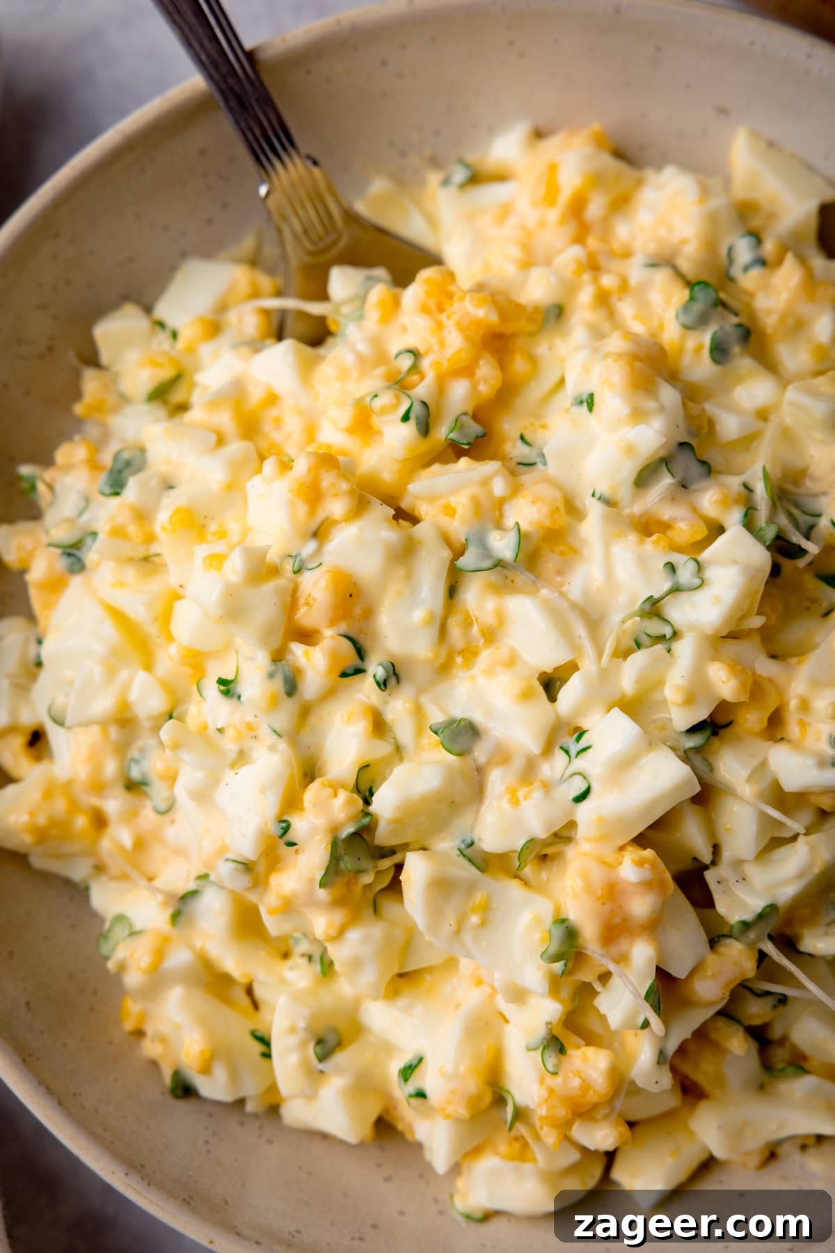 Creamy Egg Mayo Sandwich Recipe for Quick Meals 5 Tall overhead, close-up image of egg mayonnaise in a white bowl with a silver spoon sticking out.