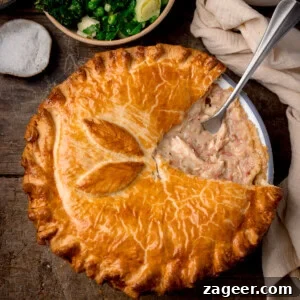 Savory Chicken and Ham Pie Recipe with Flaky Crust 13 A square, overhead shot of the chicken and ham pie, with a slice taken out of it and a silver serving utensil in the filling where the piece was. In the top left corner of the image, there is a small white dish filled with sea salt flakes. To the right of that, there is a light brown bowl filled with steamed greens. In the right side of the image, there is a cream-coloured napkin tucked around the main pie dish. This is all set on a dark wooden background.
