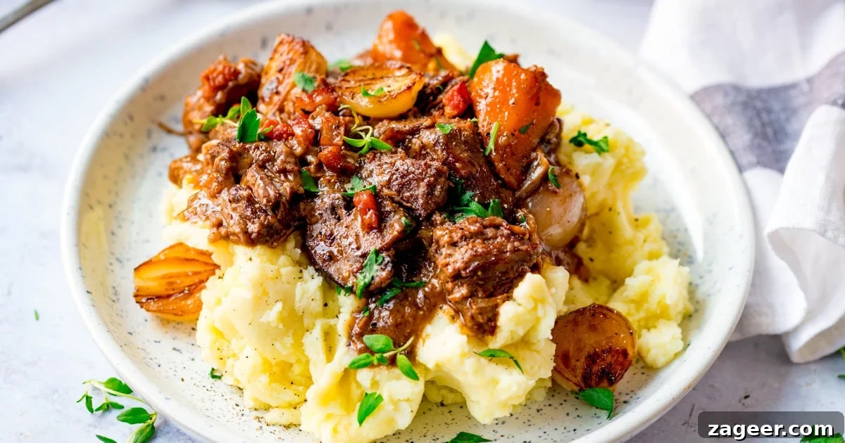 Classic Beef Bourguignon Recipe: Tender Braised Beef in Red Wine 4 A plate of mashed potato topped with beef bourguignon with carrots, onions, and garnished with chopped parsley.