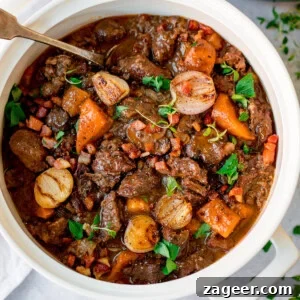 Classic Beef Bourguignon Recipe: Tender Braised Beef in Red Wine 9 A white pot filled with beef bourguignon containing chunks of beef, carrots, pearl onions, and garnished with parsley. A serving spoon rests inside the pot.