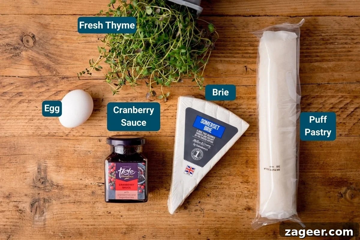 Cranberry and Brie Bites: Savory Holiday Appetizer Recipe 4 Labelled ingredients for cranberry brie bites, including an egg, a jar of cranberry sauce, a wedge of brie, puff pastry, and fresh thyme on a wooden surface.