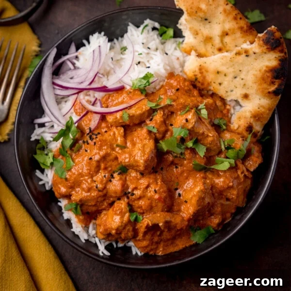 Slow Cooker Coconut Chicken Curry Recipe for Tender Meat 9 Overhead picture of a dark bowl full of boiled rice and crock pot butter chicken with some sliced red onion and charred naan bread in the corner of the bowl.