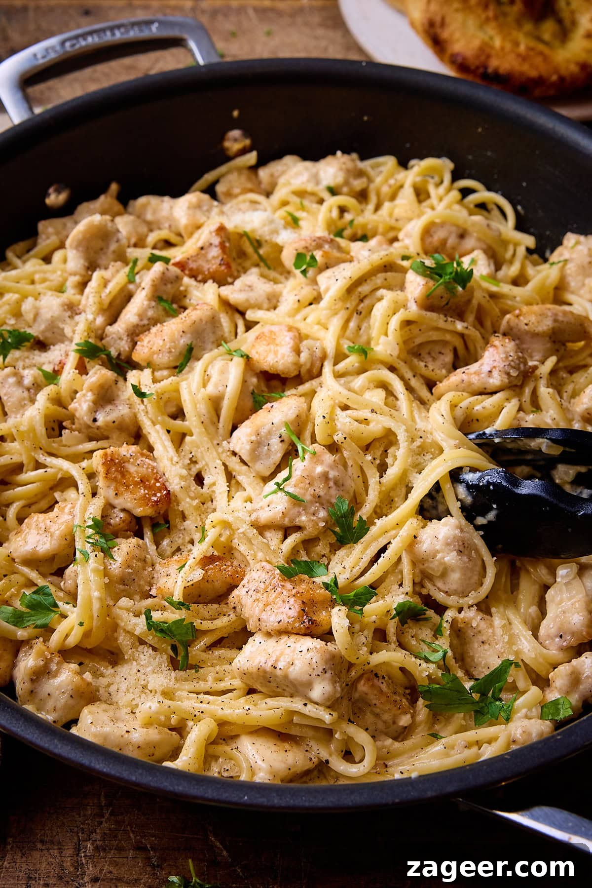 Close up picture of garlic parmesan chicken pasta in a dark grey pan sat on a wooden table.