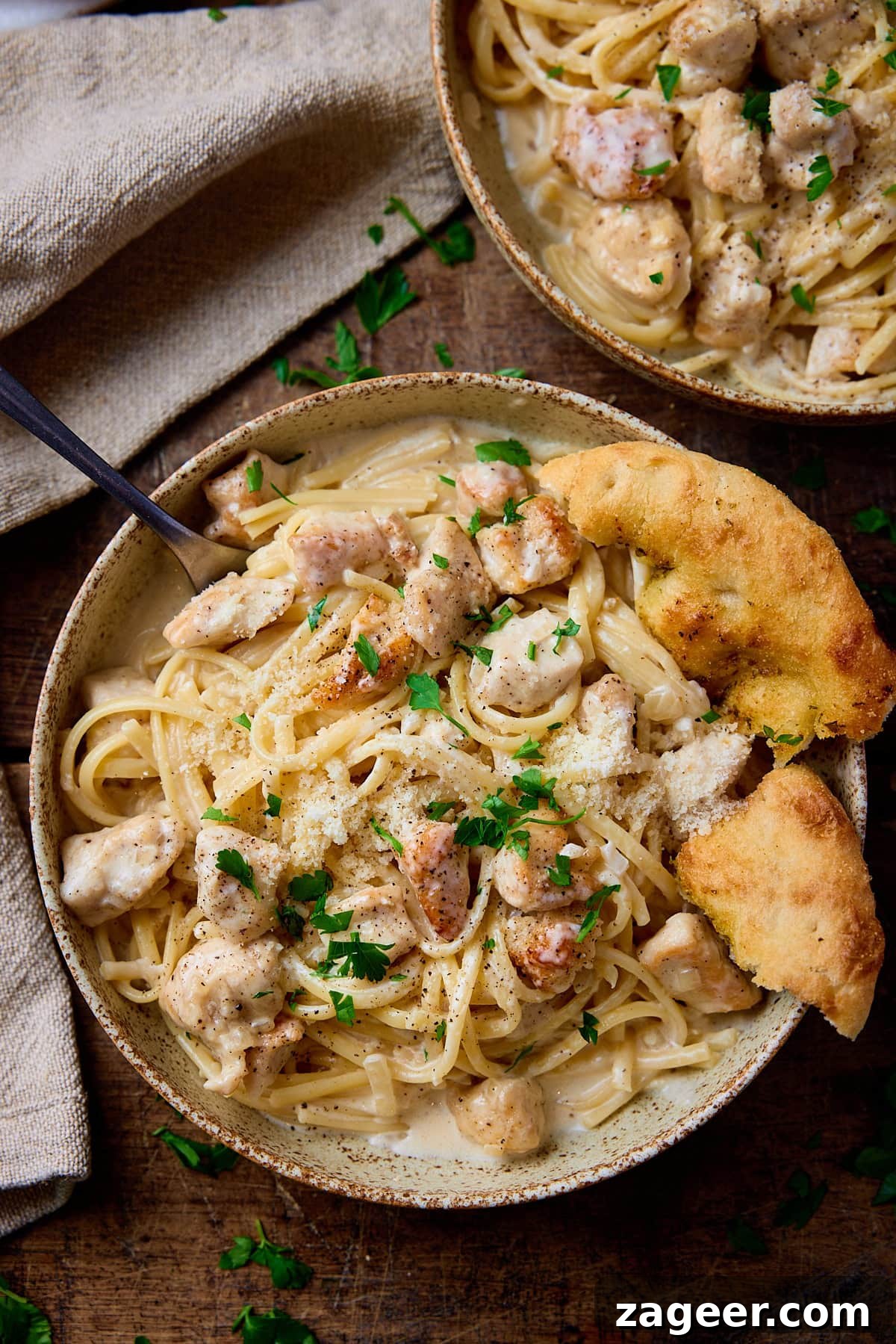 Overhead picture of a stoneware bowl on a wooden board, the bowl is full of pasta and chicken in a garlic parmesan sauce.