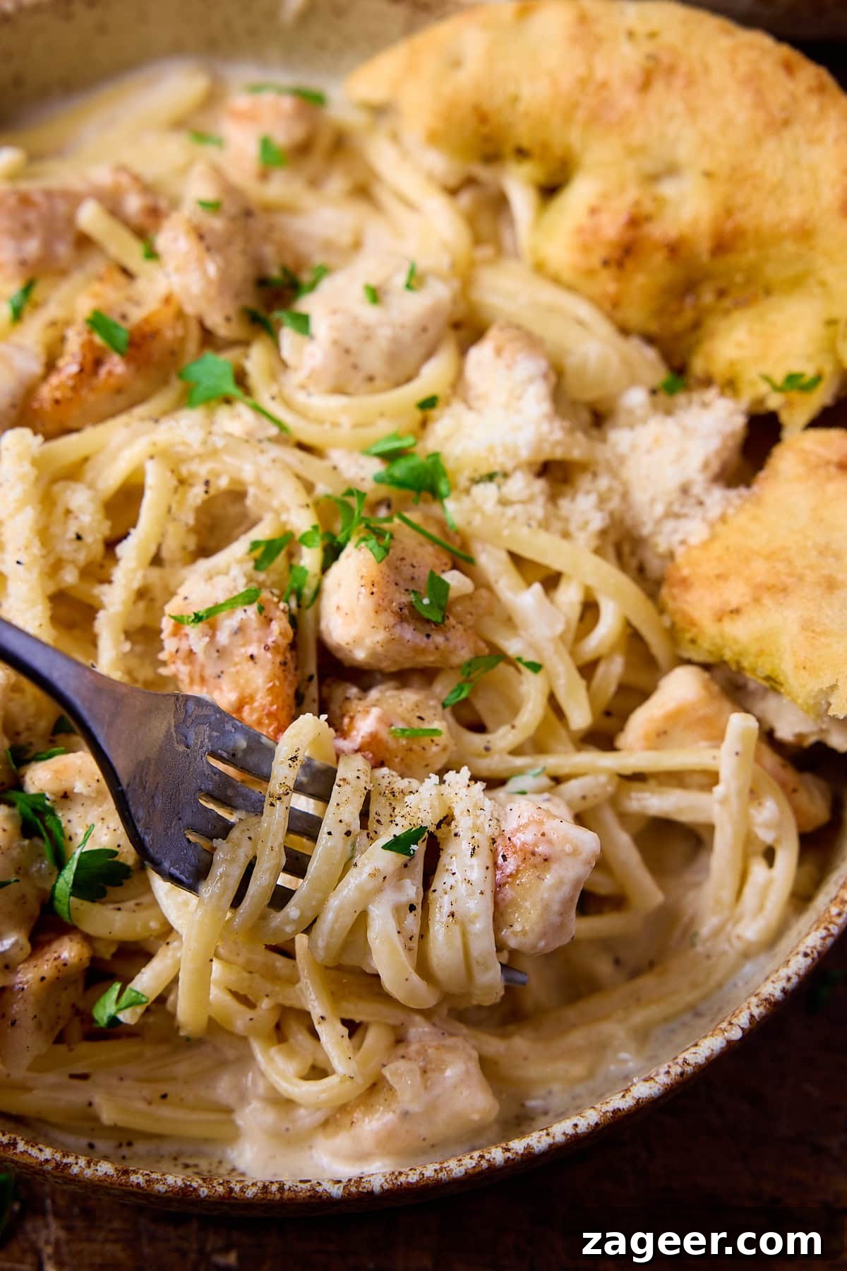 A close up picture of a dark fork full if garlic parmesan chicken pasta.