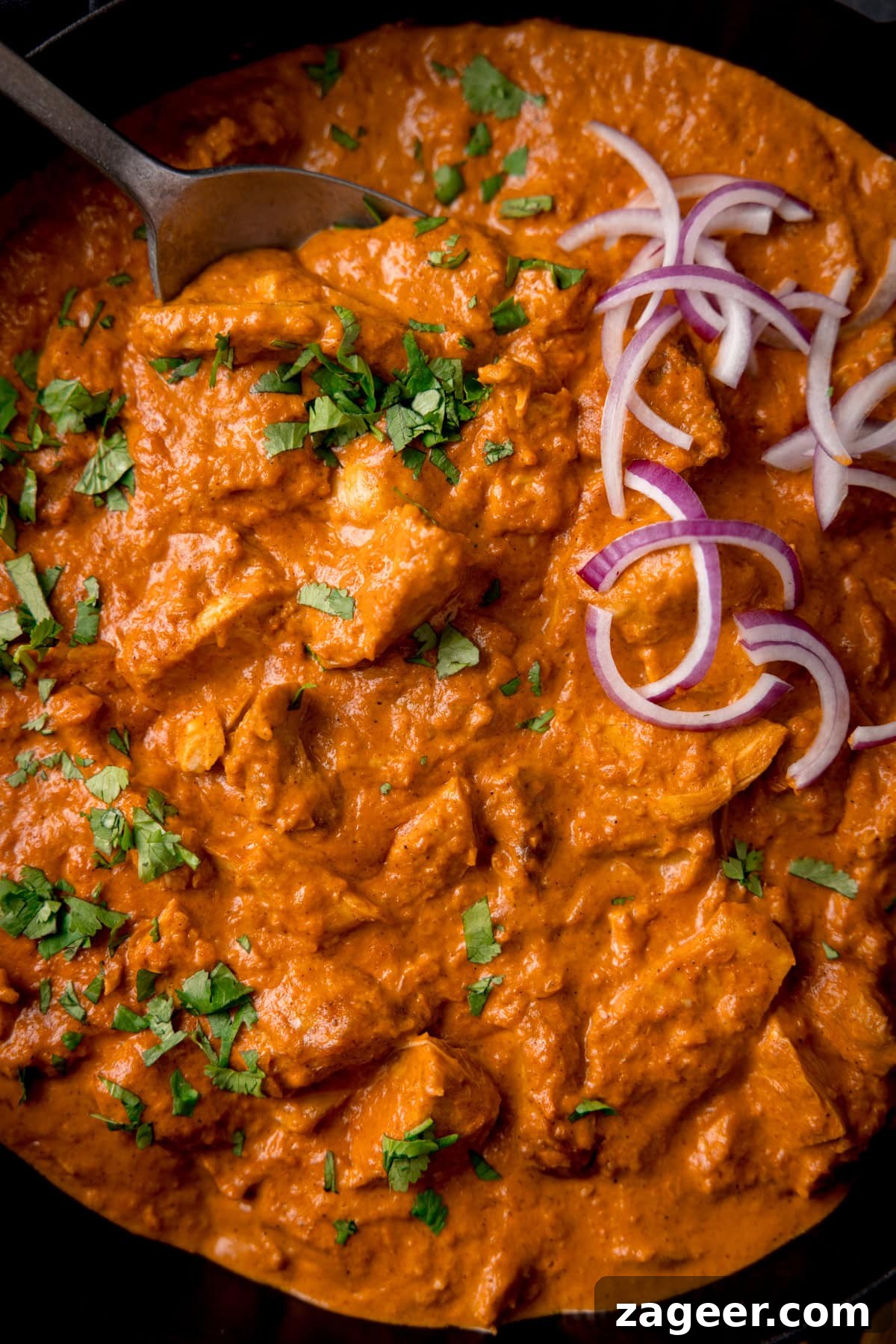 Leftover Turkey Curry Recipe: Flavorful Makeover for Leftovers 5 A tall, closeup shot of leftover turkey curry in a black skillet. The curry is topped with chopped coriander and red onion, and there is a silver spoon sticking out of the left side of the dish.