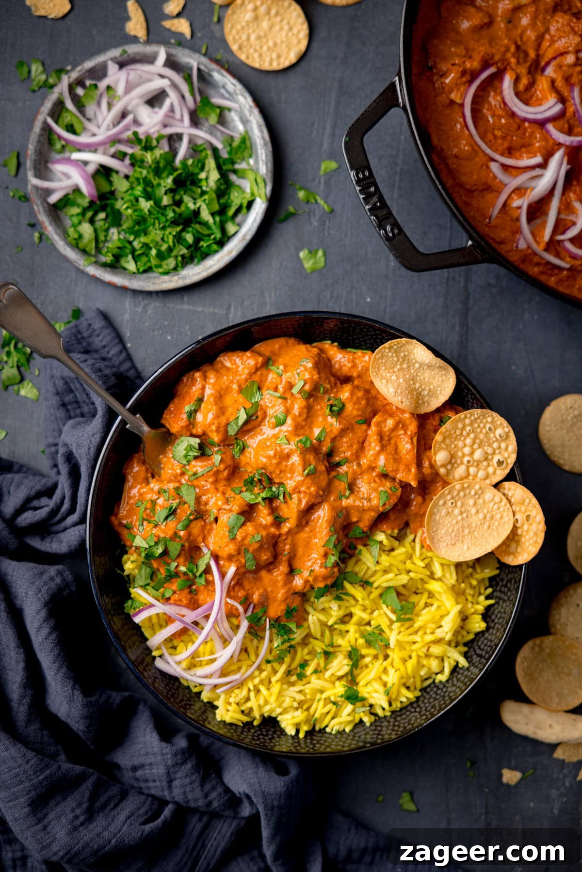 Leftover Turkey Curry Recipe: Flavorful Makeover for Leftovers 6 A tall, overhead shot of Leftover Turkey Curry served with pilau rice, topped with chopped coriander, red onions and some mini popadoms in a black bowl.