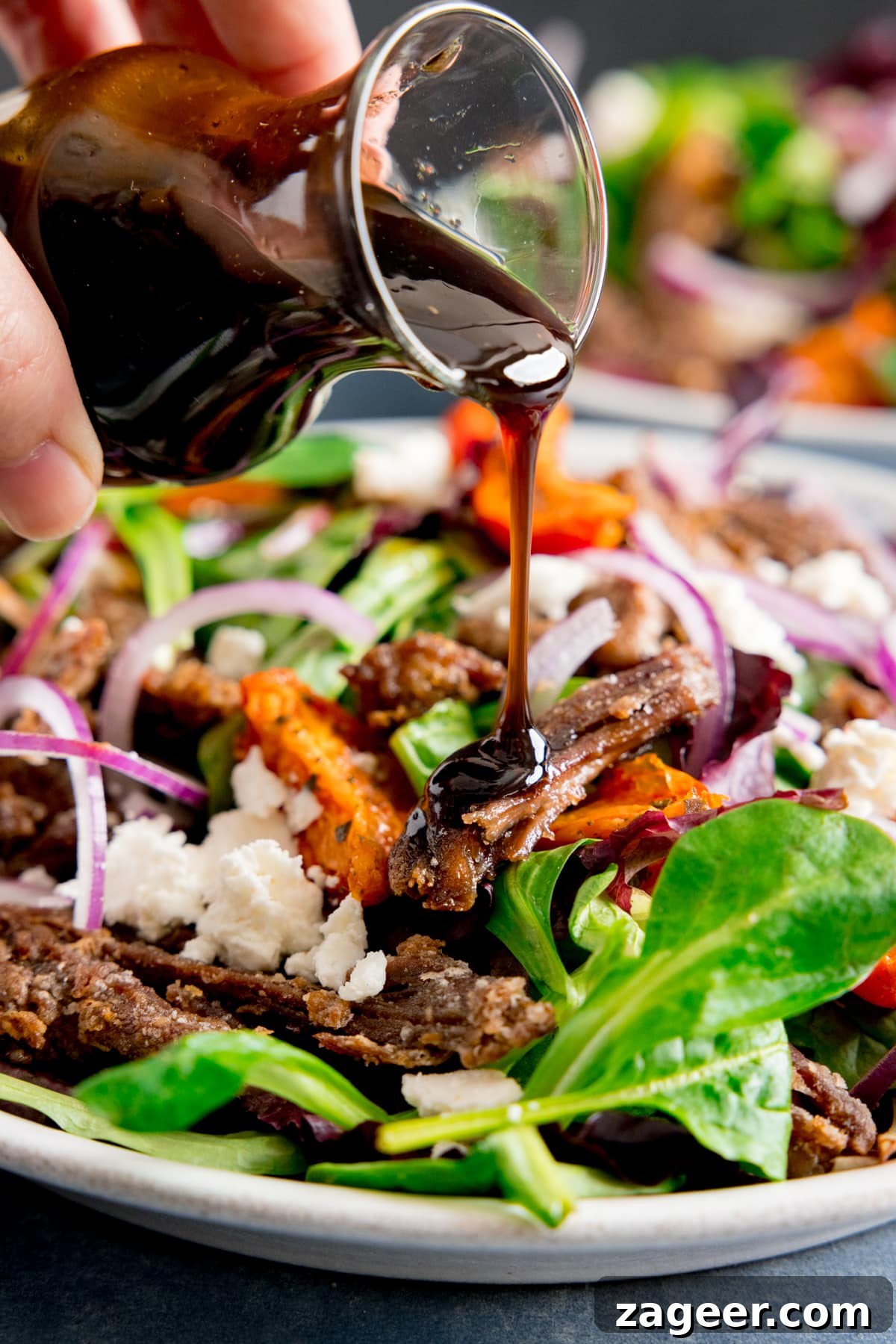 Crispy Lamb Salad with Lemon Mint Dressing 7 Close up of balsamic dressing being poured from a glass jar onto a crispy lamb, tomato and feta salad.