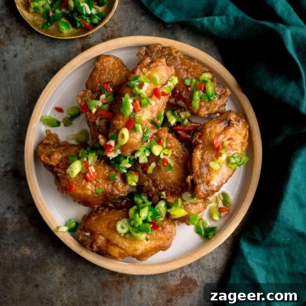 Crispy Garlic Parmesan Chicken Wings Recipe 12 Square overhead image of crispy salt and pepper chicken wings on a white plate on a rustic metal surface. There is a green napkin and a small gold dish with some of the chilli-salt-pepper topping in it.