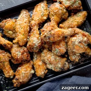 Crispy Garlic Parmesan Chicken Wings Recipe 17 A square, overhead shot of a pile of Garlic Parmesan Chicken Wings on a black rectangular baking tray. In the bottom right corner of the image, you can see a dark grey napkin tucked beneath the tray. This is all set on a dark grey background.