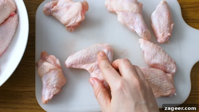 Crispy Garlic Parmesan Chicken Wings Recipe 5 Chicken wings about to be cut into two pieces on a white chopping board