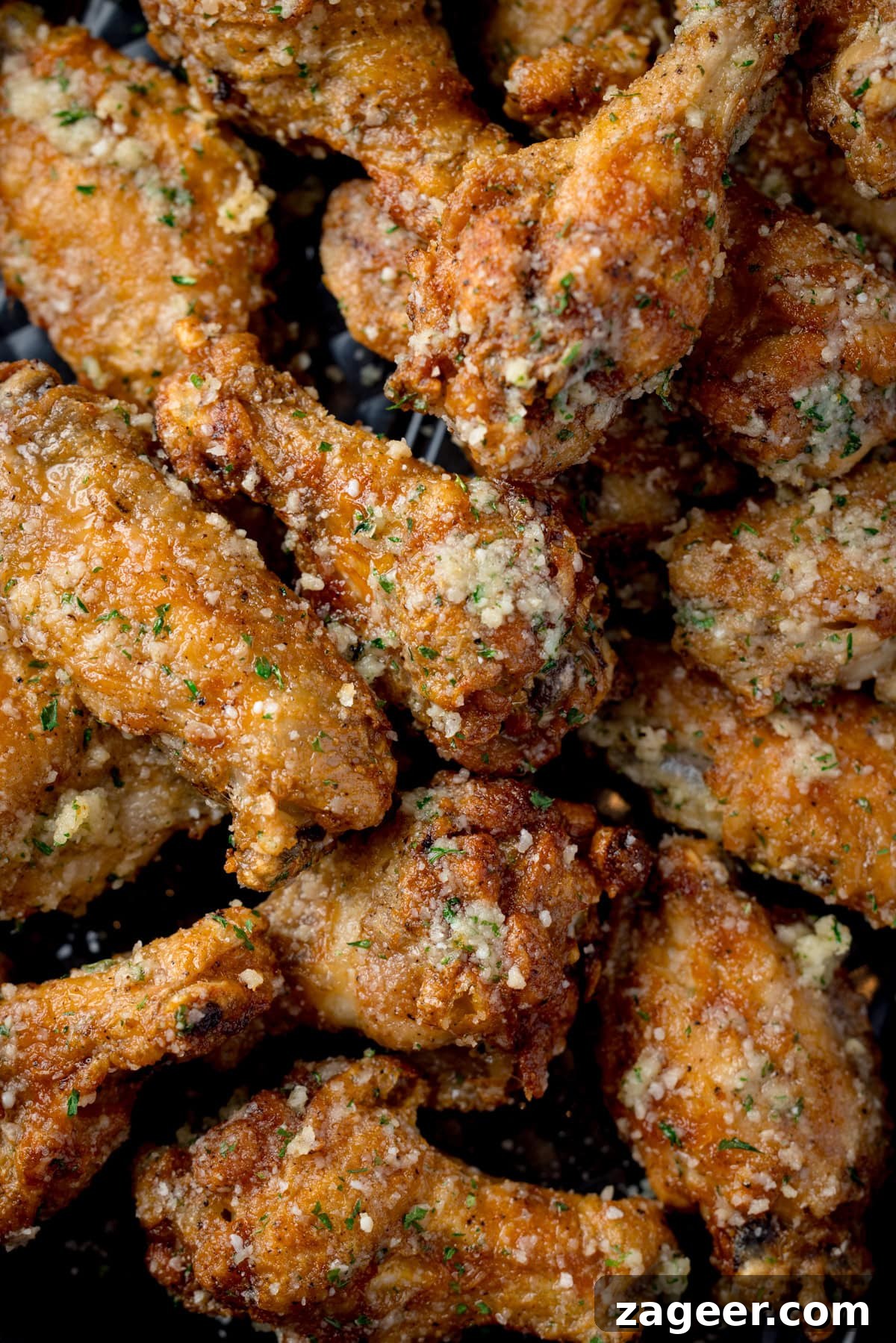 Crispy Garlic Parmesan Chicken Wings Recipe 9 A tall, closeup shot of a pile of Garlic Parmesan Chicken Wings on a black rectangular baking tray.