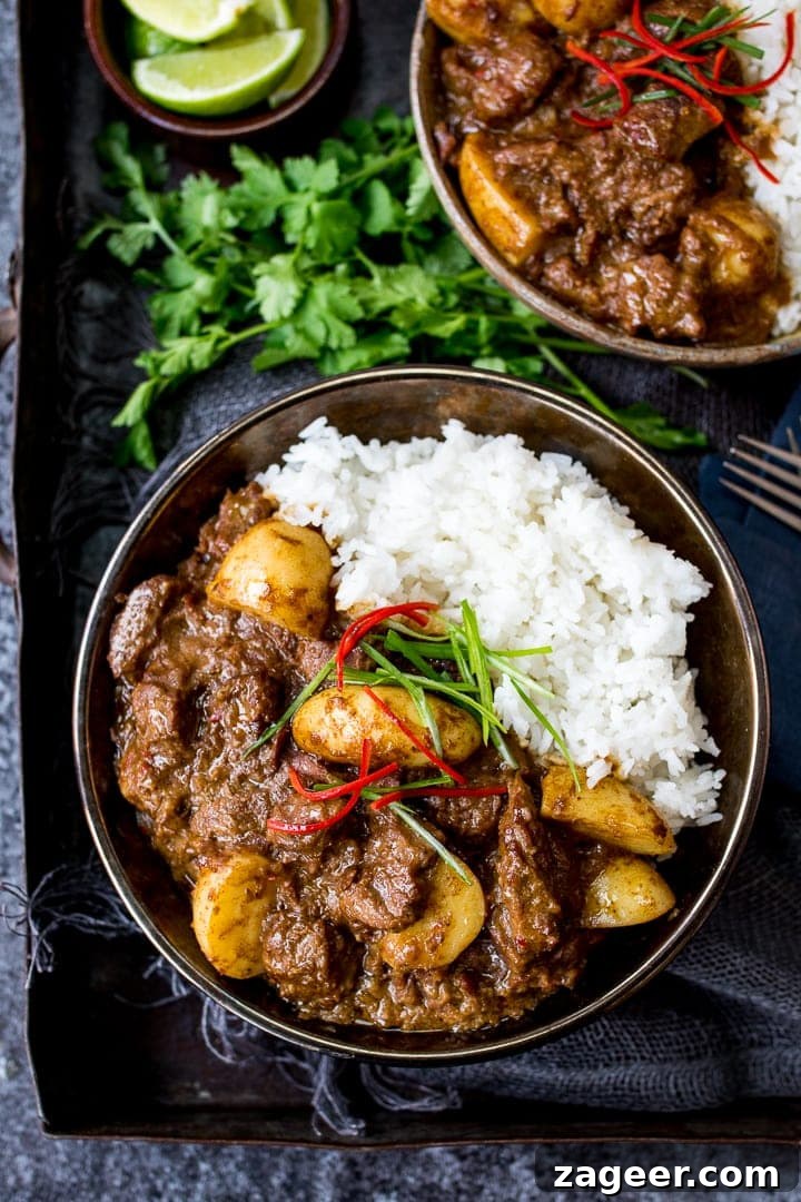 Authentic Thai Beef Massaman Curry Recipe for Home Cooking 2 Overhead photo of Slow Cooked Beef Massaman Curry in a bowl served with Rice topped with thin strips of chilli