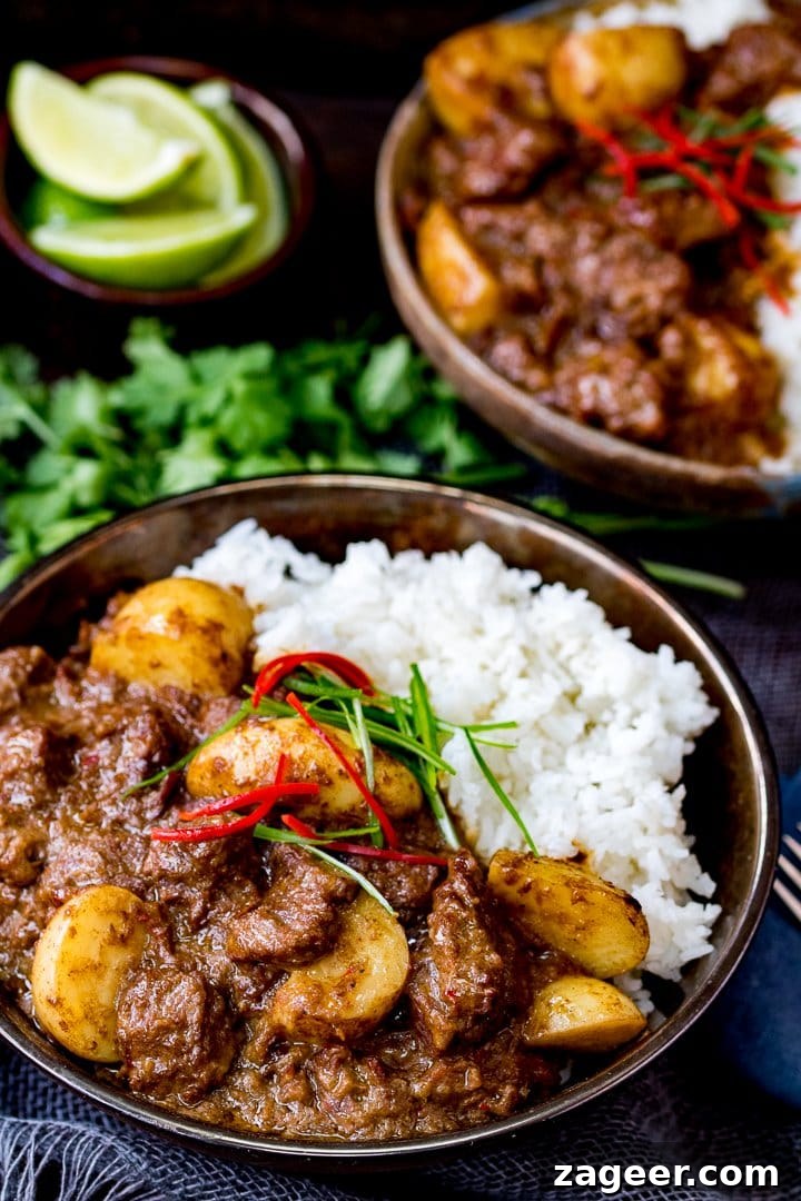 Authentic Thai Beef Massaman Curry Recipe for Home Cooking 7 Overhead photo of Slow Cooked Beef Massaman Curry in a bowl served with Rice topped with thin strips of chilli and spring onion. Fresh coriander in the background.