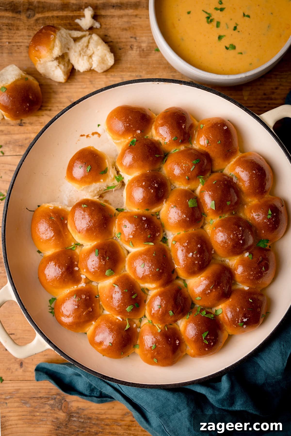 How to Make Soft, Chewy Dough Balls for Any Recipe 2 A round cast iron pan filled with golden-brown dough balls, garnished with chopped parsley and salt. The pan is set on a wooden table beside a bowl of beer cheese dip and a dark cloth serviette.