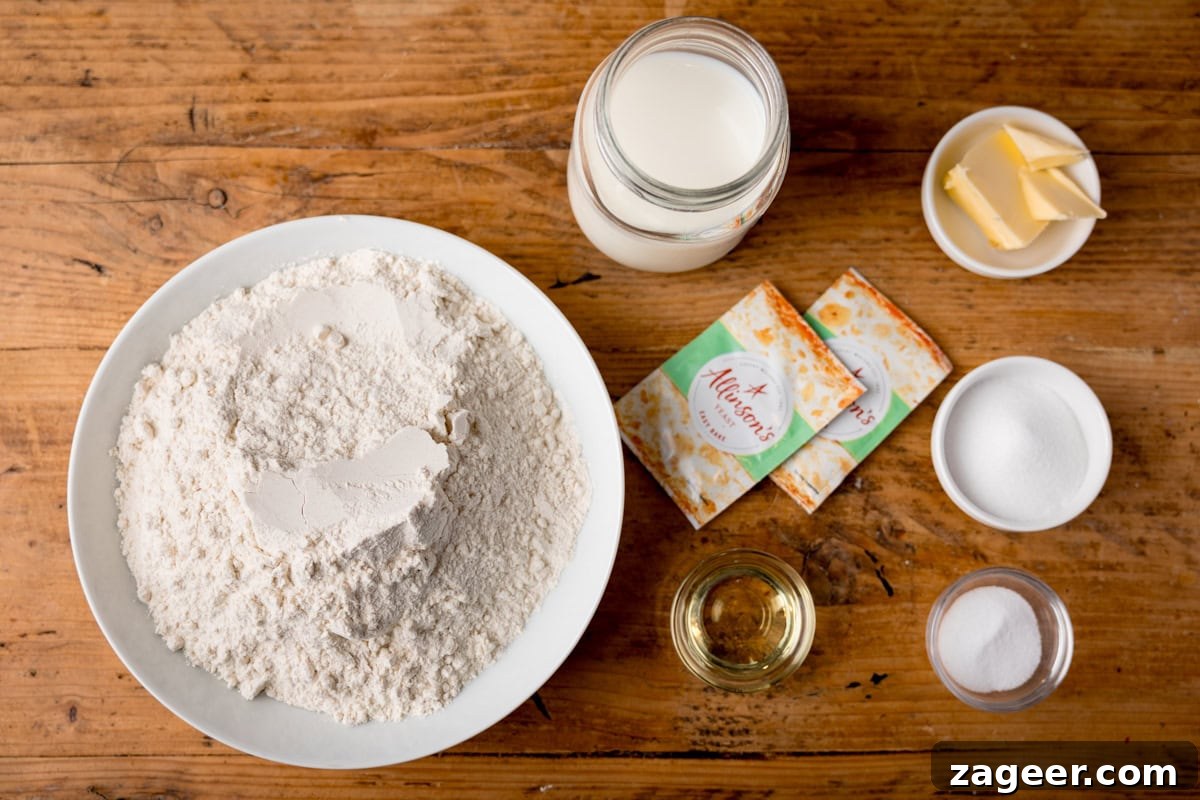 How to Make Soft, Chewy Dough Balls for Any Recipe 3 Overhead view of baking ingredients for dough balls on a wooden table: a bowl of flour, a jar of milk, blocks of butter, small dishes of sugar and salt, measuring jug with oil, and two packets of yeast.