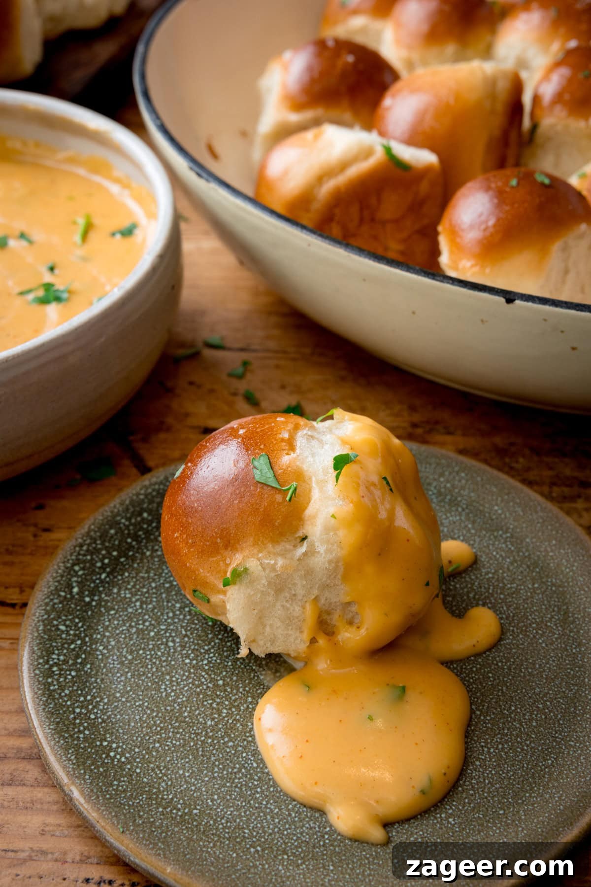 How to Make Soft, Chewy Dough Balls for Any Recipe 5 A close-up of a dough ball, on a green plate topped with creamy orange beer-cheese sauce and garnished with parsley. More dough balls are visible in the background, in a white dish. A bowl of cheese sauce sits beside it on a wooden table.