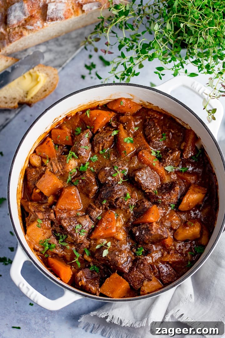 Slow-Cooked Scottish Beef Stew Recipe for Rich, Hearty Flavor 6 Large white pan filled with Scottish beef stew on a light background. Bread and fresh herbs also in scene.