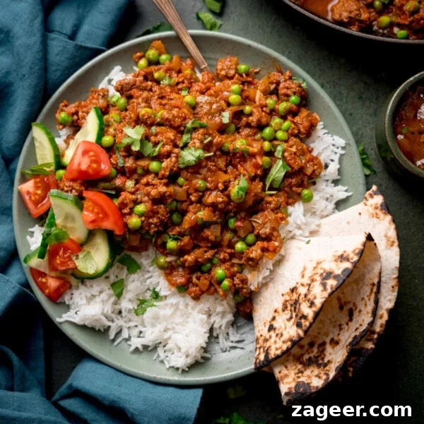 Authentic Lamb Rogan Josh Recipe: Flavorful Kashmiri Curry 6 Overhead picture of a bowl full of Keema Curry sat on a bed of boiled basmati rice with a toasted chapati folded and wedged in the side of the dish.