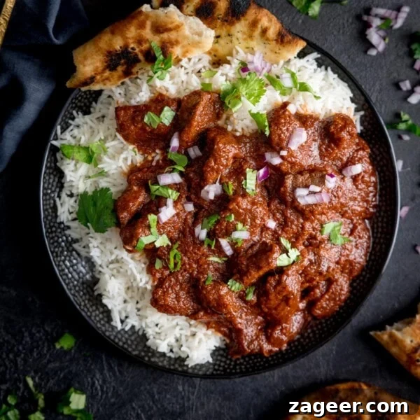 Authentic Lamb Rogan Josh Recipe: Flavorful Kashmiri Curry 7 Square overhead image of slow cooked beef madras in a black bowl with rice and pieces of naan bread.