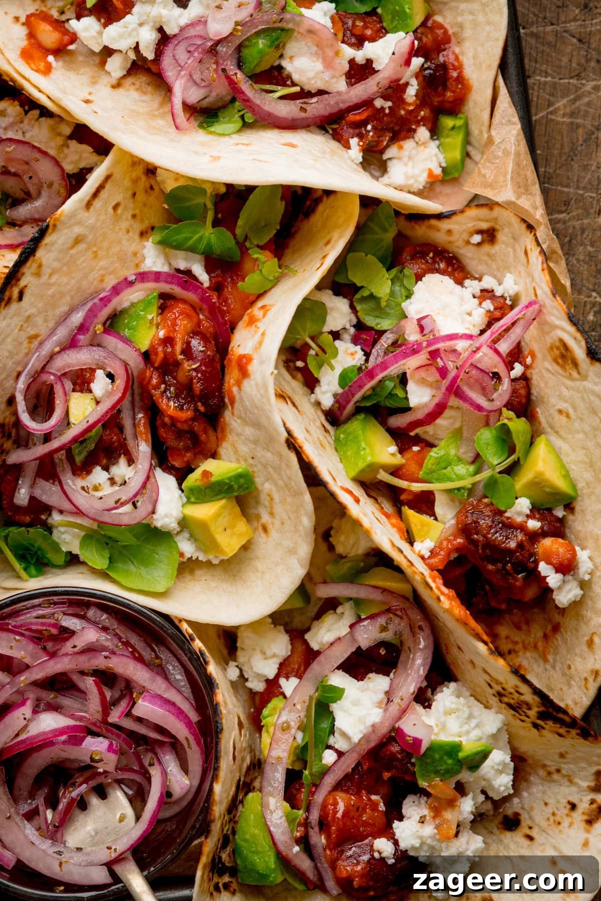 Spicy Black Bean Tacos with Fresh Salsa and Lime 9 Close up of spicy bean tacos with beans, crumbled cheese, avocado chunks, and pickled red onions are served on a tray.