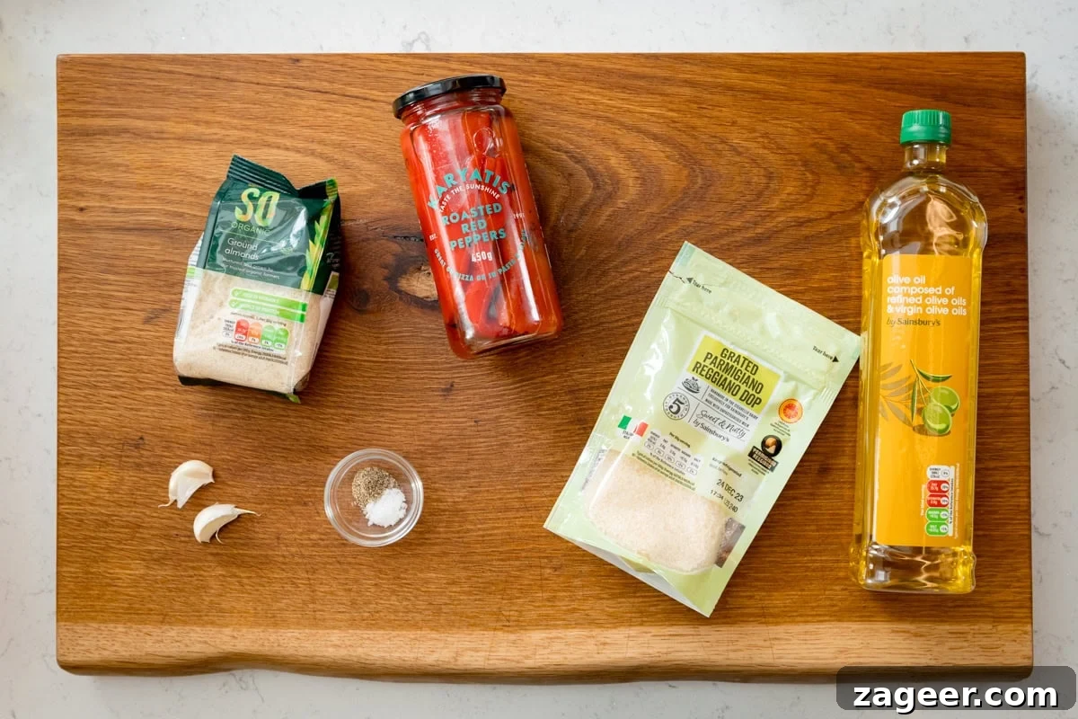 Roasted Red Pepper Pesto Recipe for Pasta, Sandwiches & Dips 3 Ingredients for red pepper pesto on a wooden board - including garlic cloves, salt, pepper, ground almonds, parmesan, olive oil and a jar of roasted peppers.