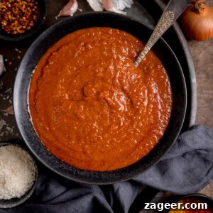 Creamy Coconut Curry Sauce Recipe for Authentic Flavor 12 A black bowl filled with coconut curry sauce, hinting at a quick easy beef curry, surrounded by garlic, onion, spices, and a cloth on a wooden surface.