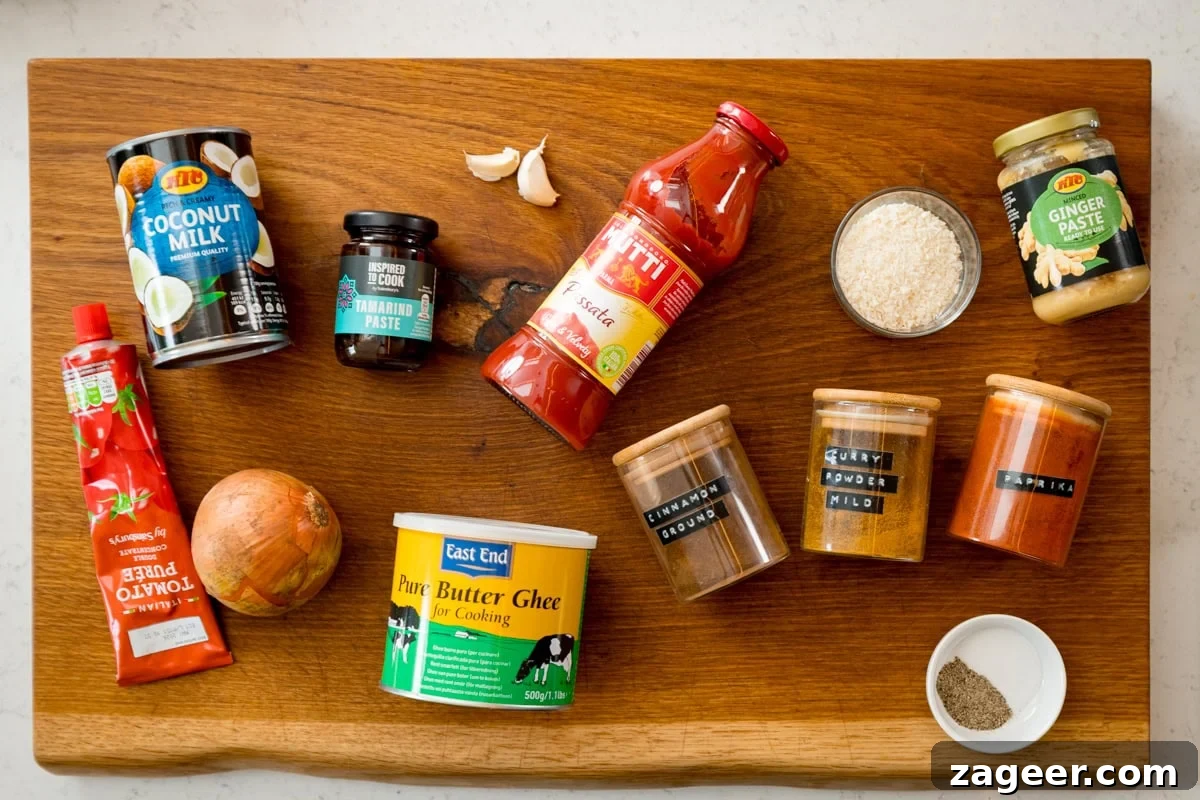 Creamy Coconut Curry Sauce Recipe for Authentic Flavor 3 Ingredients for coconut curry sauce on a wooden board, featuring coconut milk, tomato purée, spices, passata, ginger purée, an onion, and garlic cloves.