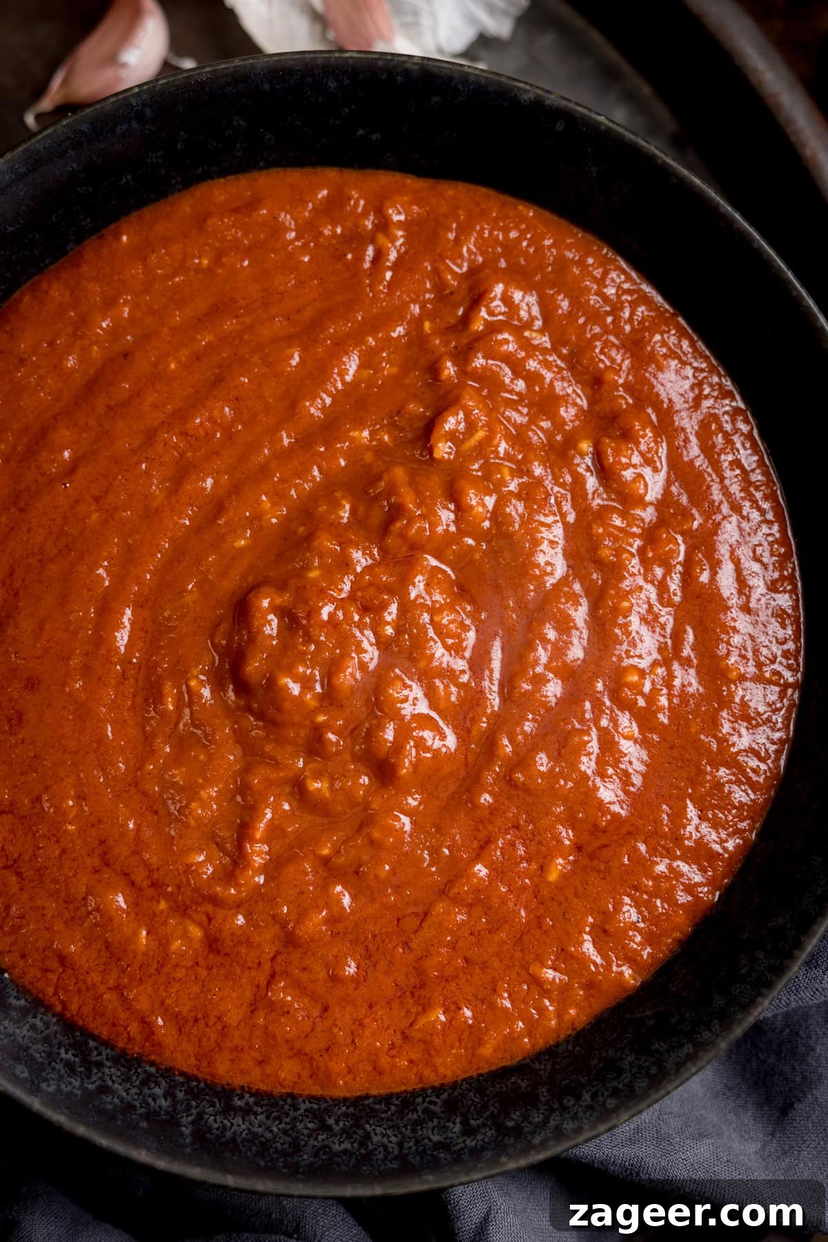 Creamy Coconut Curry Sauce Recipe for Authentic Flavor 4 Close up overhead image of a rich coconut curry sauce in a black bowl on a dark surface.