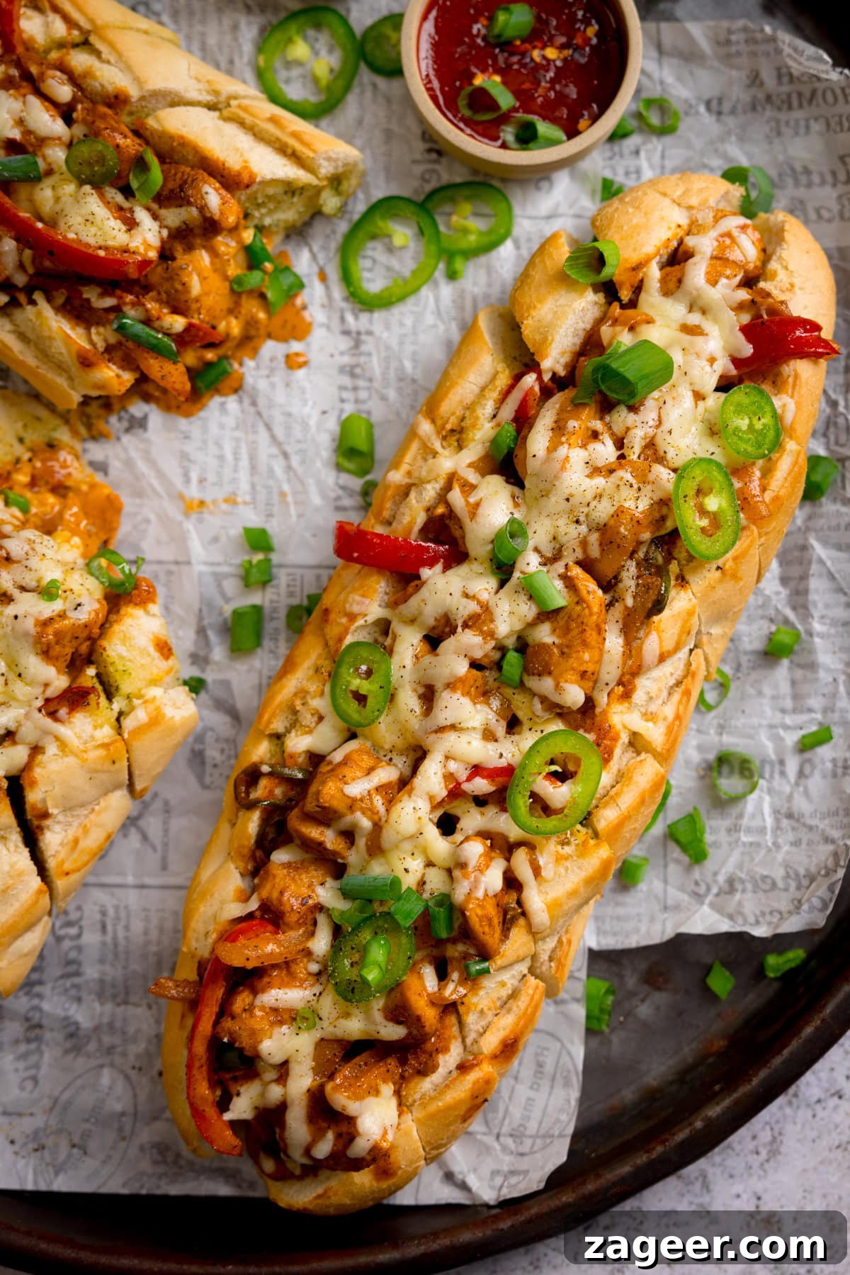 Buffalo Chicken Stuffed Garlic Bread Recipe for Game Day 5 A overhead image of Buffalo chicken stuffed garlic bread filled with melted cheese, sliced jalapeños, red peppers, and spring onions on baking parchment, served with a small bowl of sauce nearby.