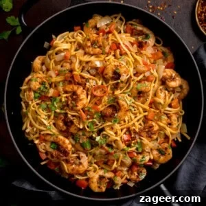 Spicy Cajun Shrimp Noodles with Garlic Butter Sauce 12 A frying pan filled with king prawn stir-fry noodles, featuring prawns, noodles, diced red peppers, onions, and garnished with chopped herbs.
