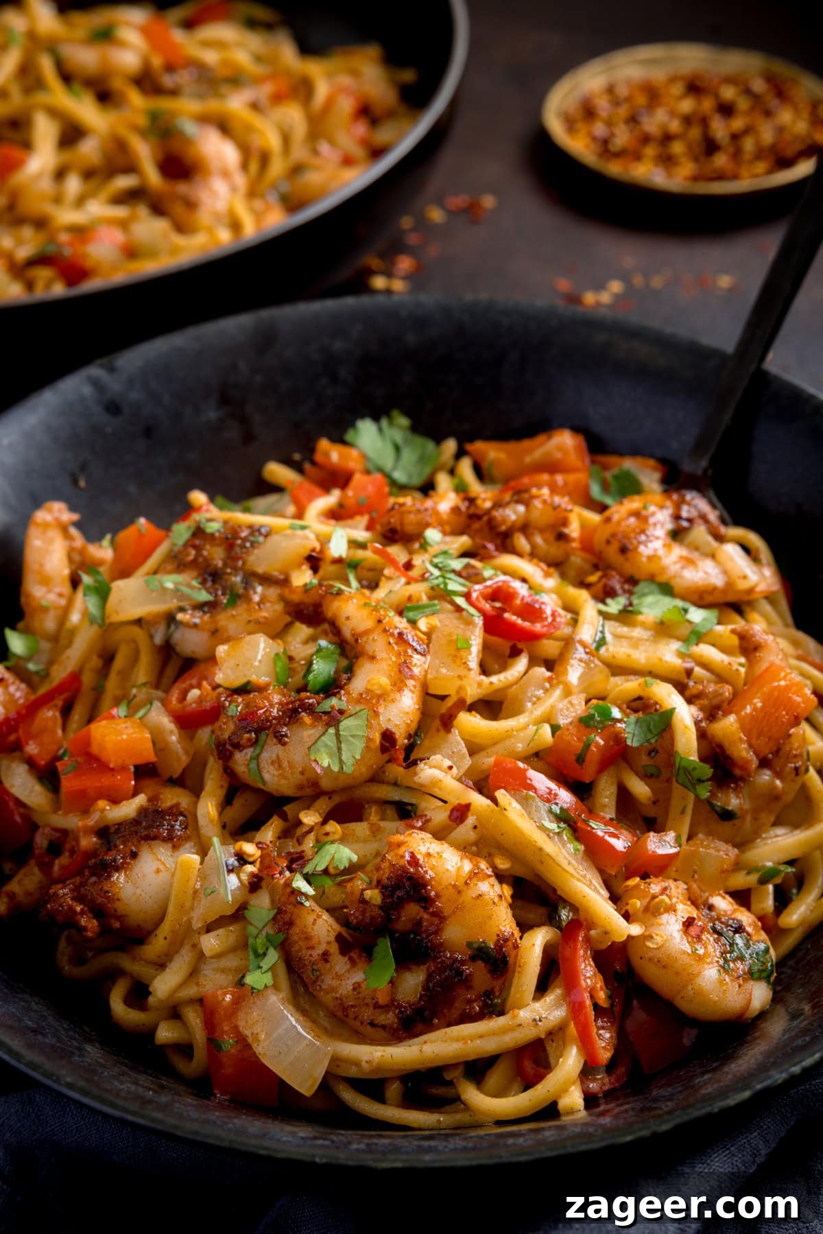 Spicy Cajun Shrimp Noodles with Garlic Butter Sauce 4 A black bowl filled with Cajun prawn noodle stir-fry, mixed with peppers, onions, and garnished with chopped coriander.