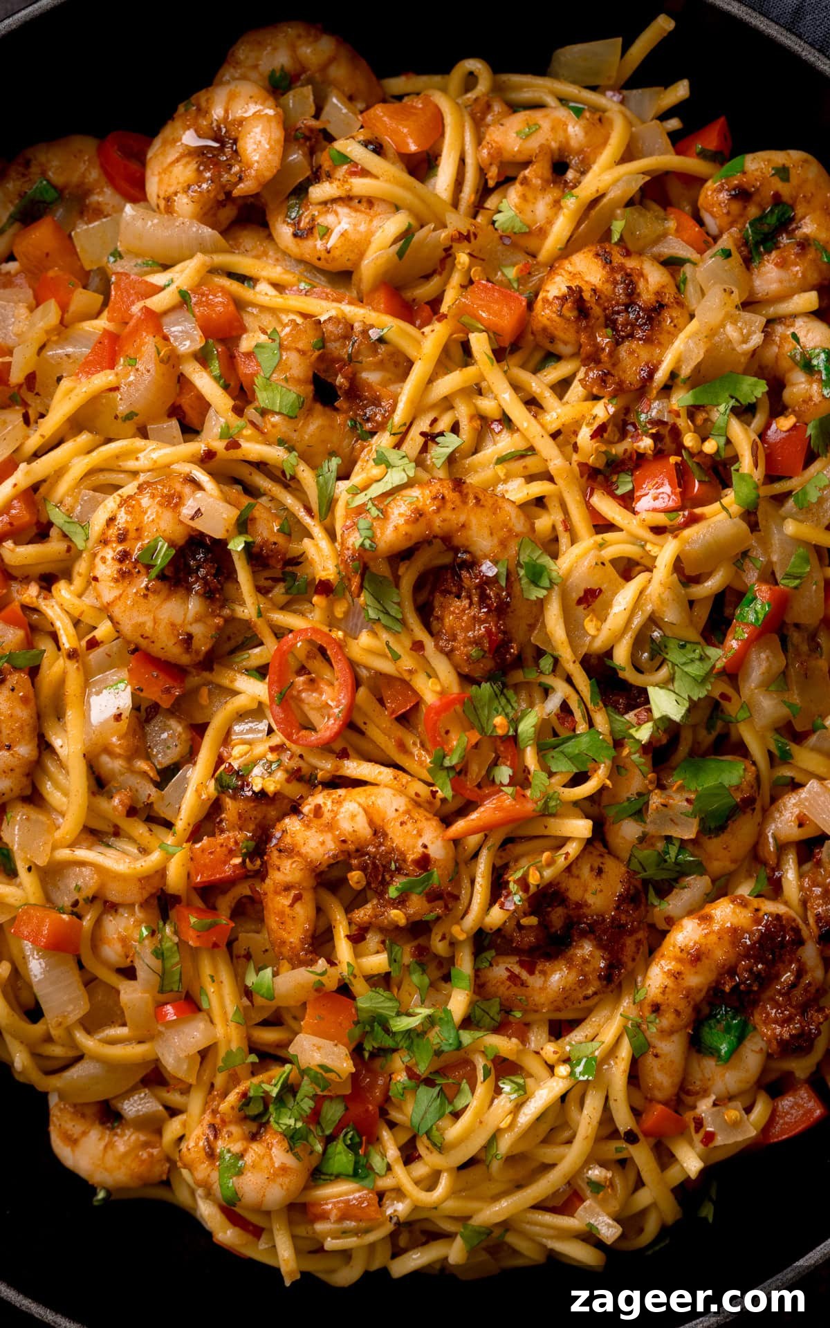 Spicy Cajun Shrimp Noodles with Garlic Butter Sauce 5 Close-up of a Cajun prawn noodle stir-fry with king prawns, red peppers, onions, and chopped coriander, garnished with chilli flakes.