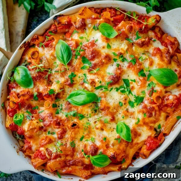 Creamy Tuna Pasta Bake with Cheesy Golden Crust 11 Sausage Pasta Bake topped with melted cheese and fresh basil leaves in a white oval dish.