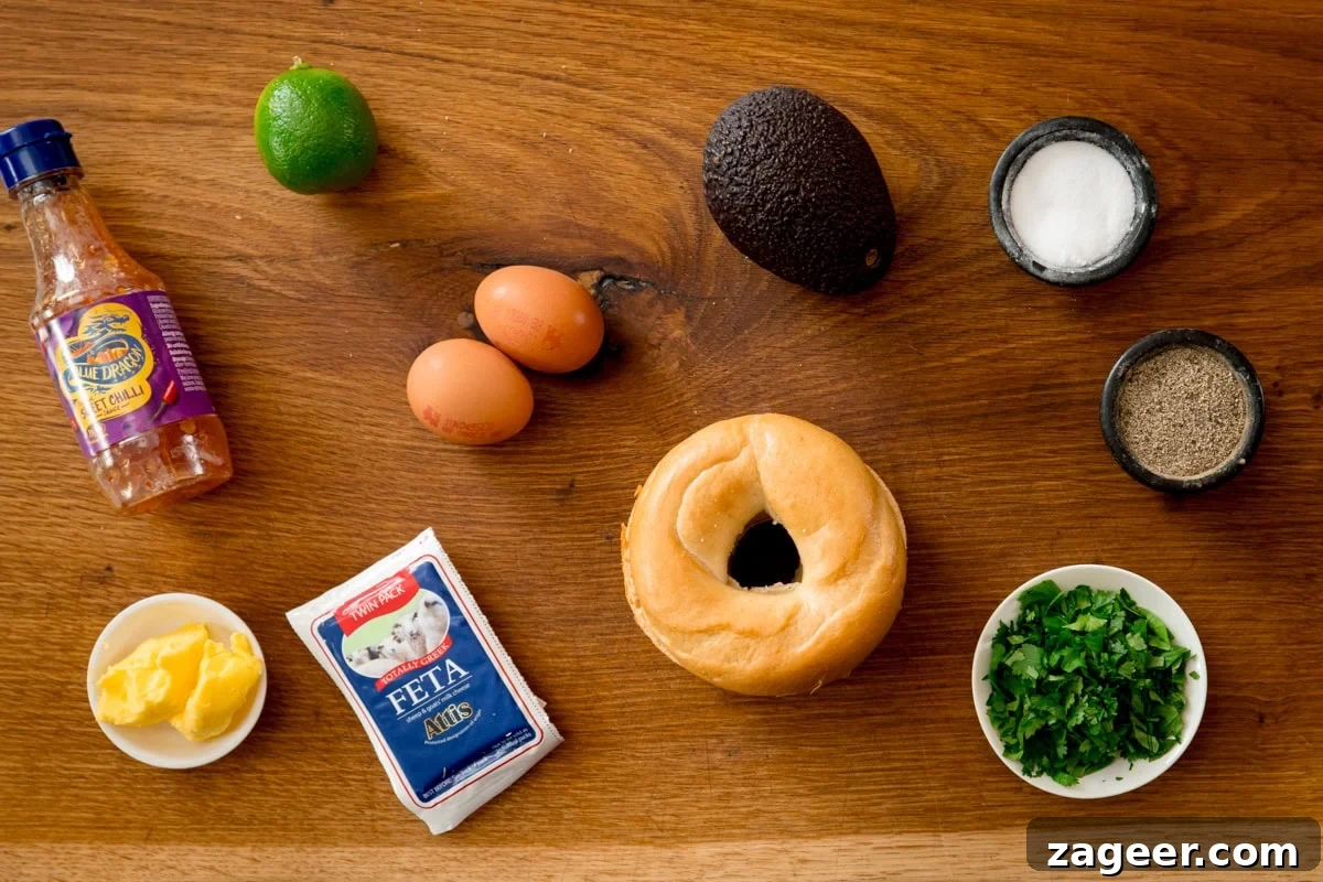Avocado and Egg Bagel Sandwich Recipe for Breakfast 3 Ingredients for avocado egg bagel on a wooden board. Including: a bagel, eggs, avocado, a lime, feta cheese, coriander (cilantro), butter, sweet chilli sauce, salt and pepper.