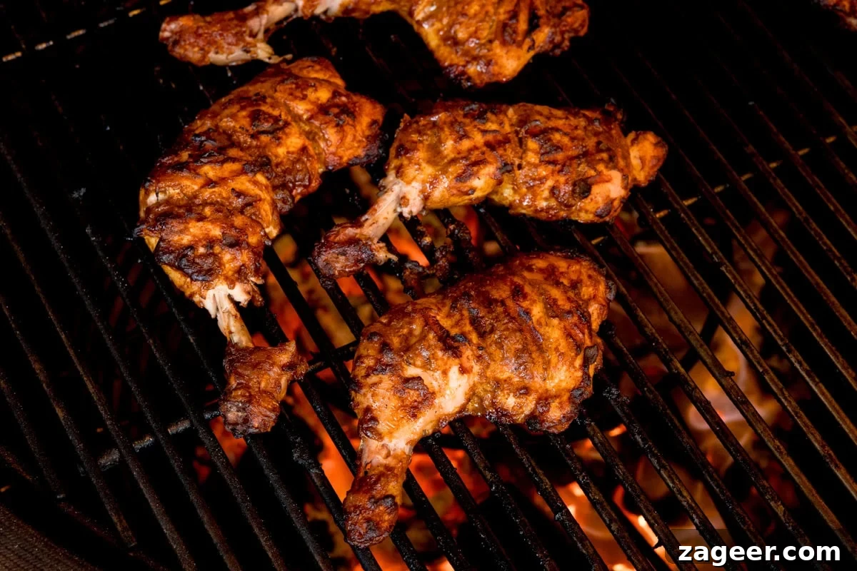 Authentic Tandoori Chicken Recipe: Flavorful Indian Grill Instructions 11 Four pieces of tandoori chicken with char marks are cooking on a barbecue over open flames.