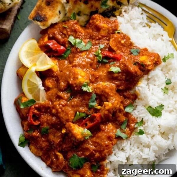 Authentic Tandoori Chicken Recipe: Flavorful Indian Grill Instructions 18 chicken pathia and boiled rice on a white plate. Curry is topped with lemon slices and coriander.