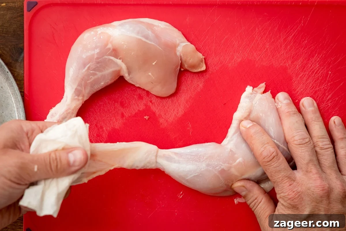 Authentic Tandoori Chicken Recipe: Flavorful Indian Grill Instructions 5 A person removes the skin from a raw chicken leg quarter on a red chopping board.