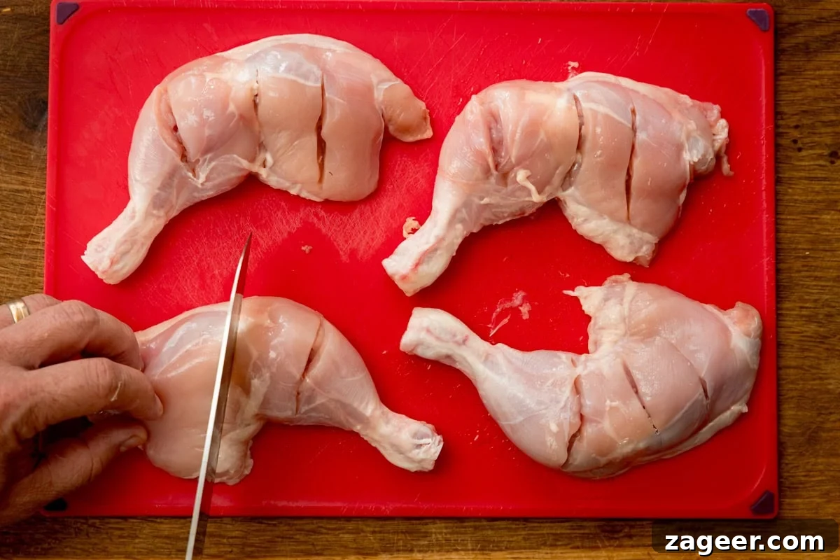 Authentic Tandoori Chicken Recipe: Flavorful Indian Grill Instructions 6 Four raw Chicken legs with incisions are on a red chopping board. A hand is holding a knife, cutting into one of the legs.