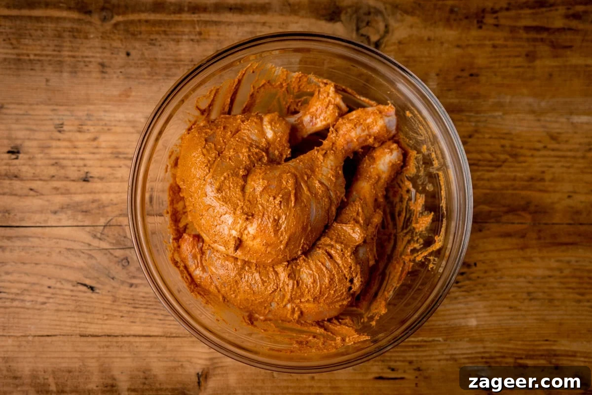 Authentic Tandoori Chicken Recipe: Flavorful Indian Grill Instructions 7 A glass bowl containing raw chicken legs coated in a tandoori marinade sits on a wooden surface.