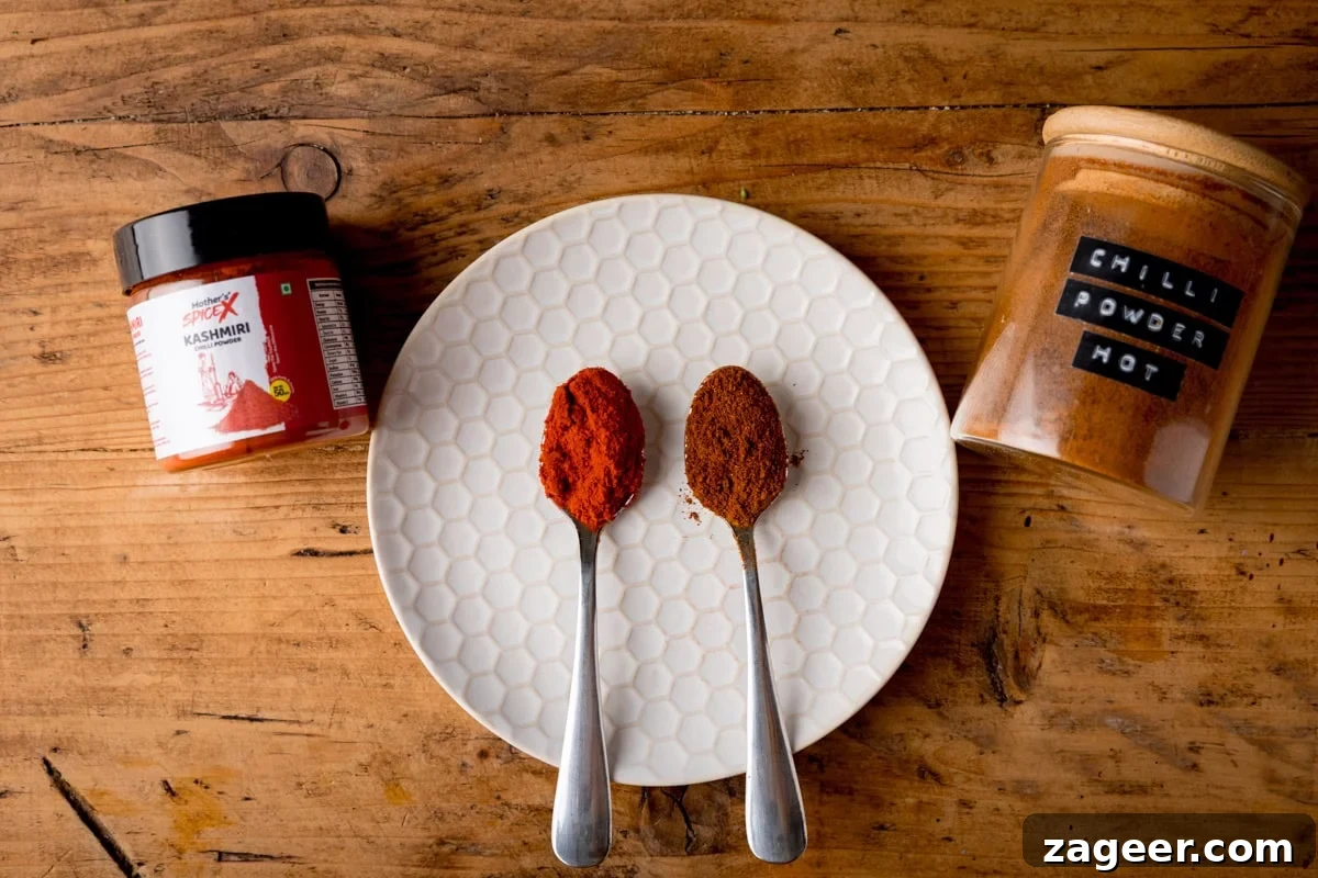 Authentic Tandoori Chicken Recipe: Flavorful Indian Grill Instructions 8 Two spoons showing the difference between regular chilli powder and kashmiri chilli powder on a white plate all on a wooden surface.