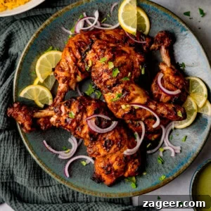 Authentic Tandoori Chicken Recipe: Flavorful Indian Grill Instructions 10 Tandoori chicken legs grilled to perfection, garnished with lemon slices, red onion, and chopped herbs on a blue plate.