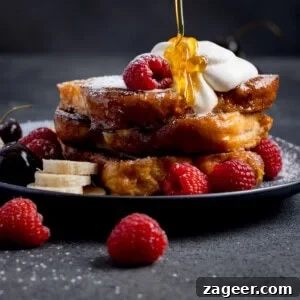 Cinnamon French Toast Recipe: Crispy, Custardy Morning Toast 7 A stack of brioche French toast topped with whipped cream, raspberries, banana slices, and cherries, with syrup being poured over the top.