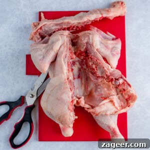 Raw butterflied chicken spatchcocked on a red chopping board, with poultry shears placed beside it.