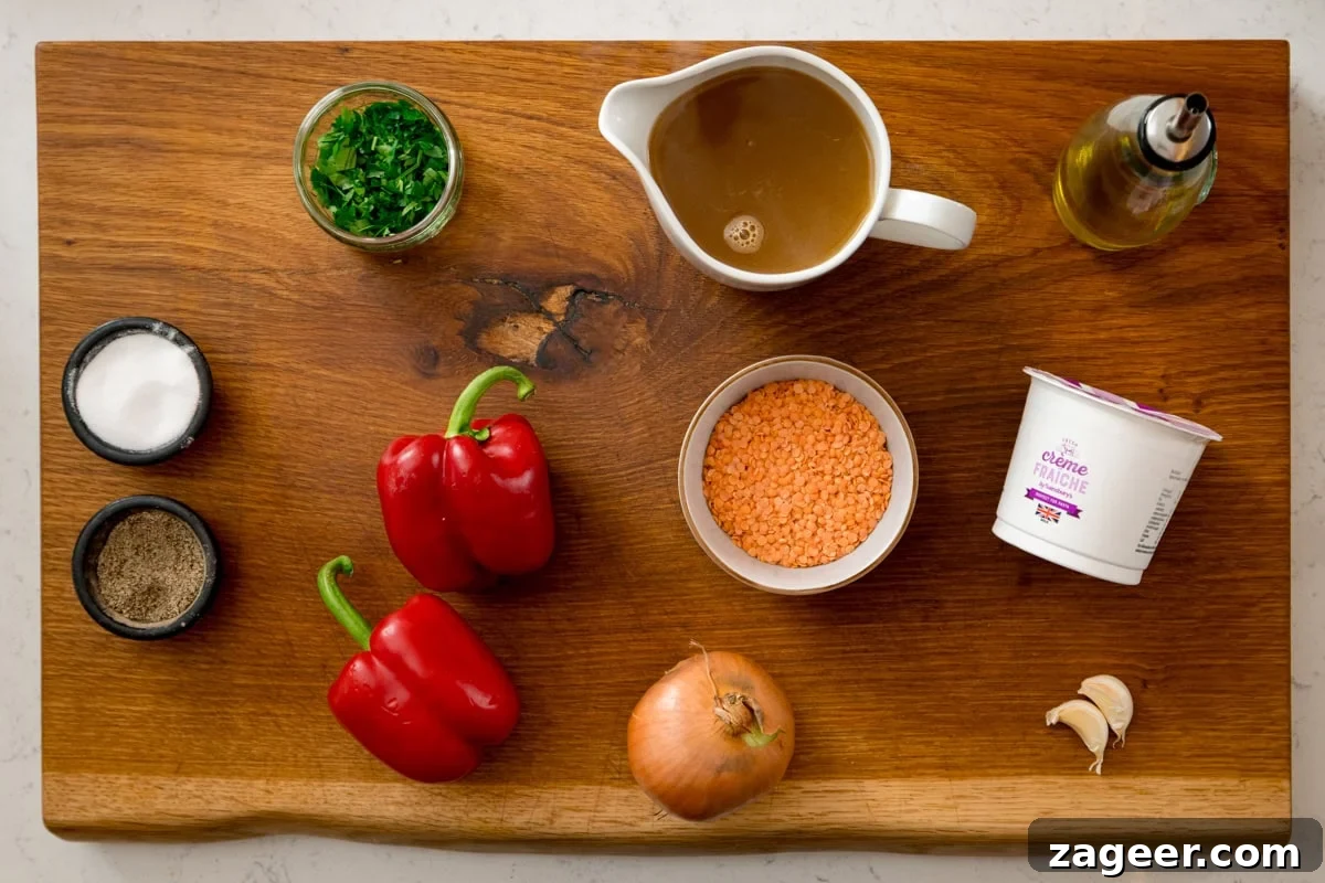 Red Pepper and Lentil Sauce Recipe for Pasta and Veggies 3 A wooden board displays ingredients for a red lentil pasta sauce: red peppers, an onion, garlic cloves, a bowl of red lentils, creme fraiche, stock, chopped herbs, olive oil, salt and pepper.