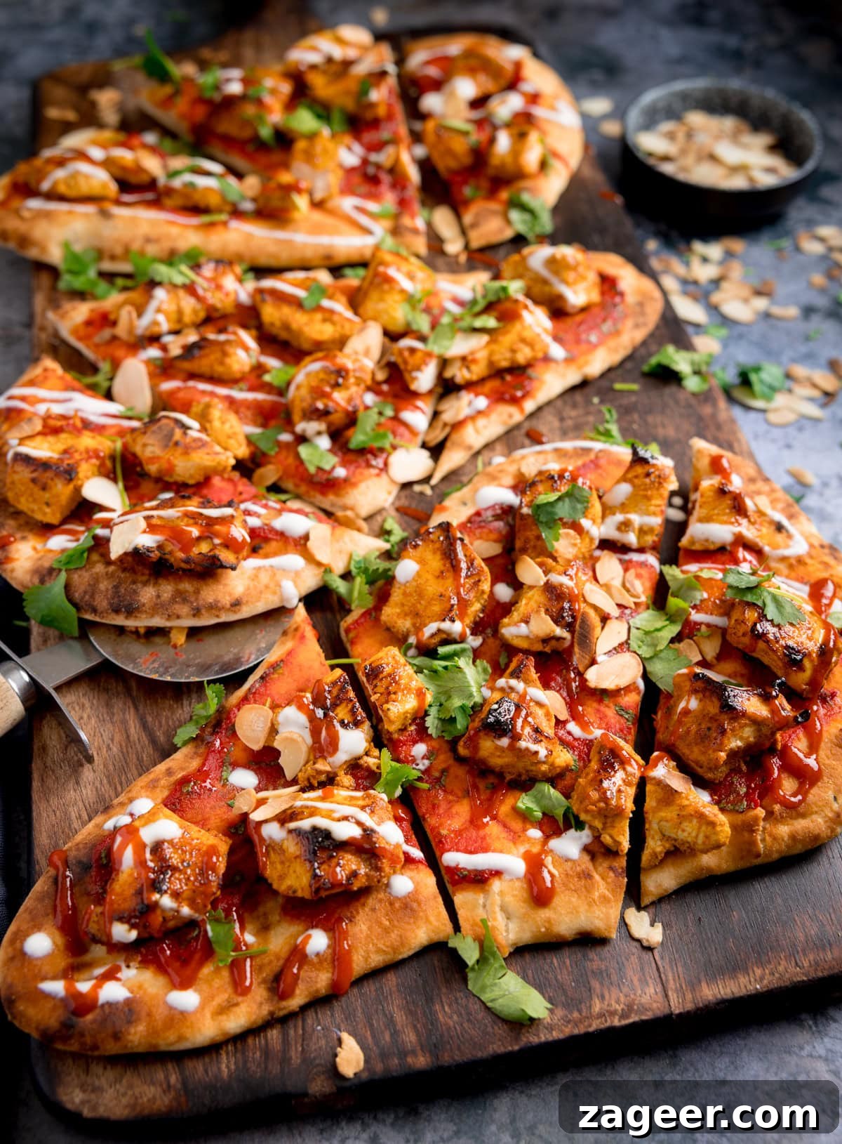 Chicken Tikka Pizza Recipe: Crispy Homemade Tandoori-Style Pizza 4 Several slices of Chicken tikka pizza topped with grilled chicken, fresh coriander, sliced almonds, and drizzles of red and white sauce, served on a wooden board.